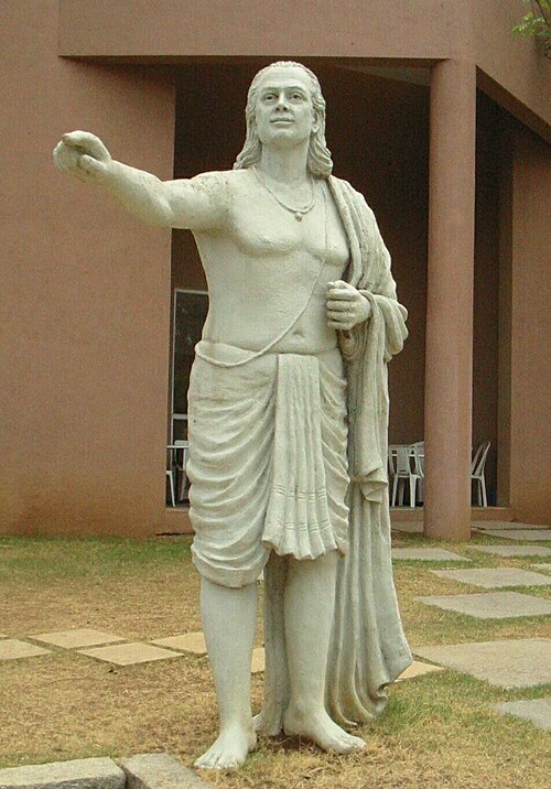 Estátua de pedra branca de Aryabhata em pé, com o braço estendido, num jardim.